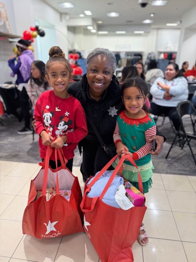 San Mateo PAL officer smiling with two children at a community event.